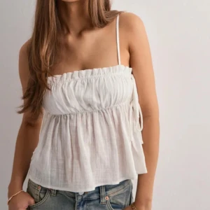 Vit linnetopp med knytband - Supersöt vit linnetopp med tunna axelband och volangkant upptill. Toppen har justerbara axelband och knytning i sidorna för en extra detalj. Luftigt material som passar perfekt till jeans eller kjol. Lapparna kvar,  Slutsåld på hemsidan🌷pris kan diskuteras 