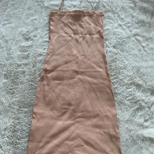 Beige ribbad klänning från Zara - Supersnygg beige ribbad klänning från Zara med smala axelband och figurnära passform. Klänningen är kort och har en enkel, stilren design som passar perfekt till varmare dagar. Materialet är mjukt och stretchigt för en bekväm känsla.
