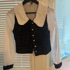 Svartvit kavajjacka från NewYorker  - Stilren svartvit kavajjacka från NewYorker i storlek S. Jackan har vit krage och ärmar i bomull, svart mönstrad kropp med rutigt tyg och dekorativa pärlknappar framtill. 