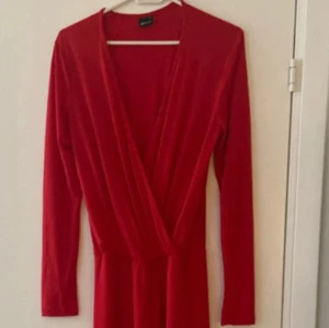 Röd jumpsuit med v-ringning - Snygg röd långärmad jumpsuit med omlott och djup v-ringning. Jumpsuiten har en figurnära passform och är perfekt för dig som vill sticka ut. Materialet är mjukt och följsamt, vilket gör den både bekväm och stilren.