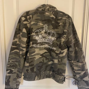 Camouflagejacka - Snygg camouflagejacka från Victoria Beckham med broderad krona och strassdetaljer på ryggen. Jackan har flera dragkedjor och nitar. Står xl i den men skulle inte säga att det stämmer. Det är mer en xs/s. Den är lite tjockare och varmare än en än jeans jacka. Några diamanter saknas där bak men det är inget som syns.