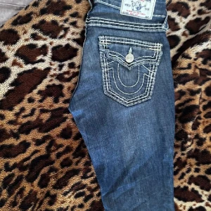 Vintage True Religion jeans - Snygga blå jeans från True Religion med tydliga vita kontrastsömmar och ikoniska fickdetaljer. Klassisk femficksmodell bootcut