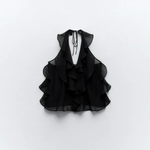 Svart volangtopp med knyt i nacken XS - Supersnygg svart topp i halvtransparent polyester med volanger framtill och längs sidorna. Djup v-ringning och knyt i nacken ger en cool look. Perfekt för dig som gillar statement-plagg med extra detaljer.