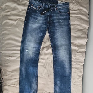 Diesel Safado blå jeans slim-straight - Snygga blå jeans från Diesel, modell Safado, med slim-straight passform. Jeansen har slitna detaljer, klassiska fem fickor och coola kontrastsömmar. Tillverkade i stretchig denim för extra komfort ✅️ Perfekta för dig som gillar en modern och avslappnad stil 🔥De är köpta för några år sedan och aldrig använda då de inte passade ‼️