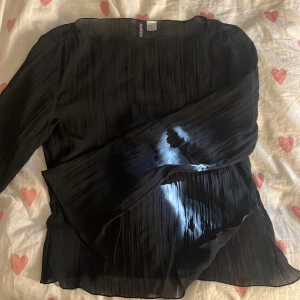 Svart blus från H&M Divided - Säljer en svart omlottblus från H&M Divided i storlek M. Blusen har plisserat tyg och långa, vida ärmar som ger en snygg flowy känsla. Perfekt för dig som gillar stilrena och trendiga plagg med lite extra detalj. Lite skir