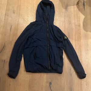 Mörkblå vindjacka från Stone Island - Snygg mörkblå vindjacka från Stone Island perfekt till våren och sommaren. Köpt på NK i Stockholm. Den har inga defekter och är inte använd så mycket. Storlek S. Köpte för 4500 
