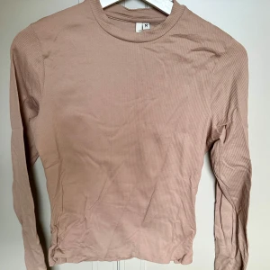 Beige ribbad långärmad tröja  - Säljer en beige ribbad långärmad tröja från Nelly i storlek M. Tröjan har en rund halsringning och är i ett mjukt, stretchigt material som sitter snyggt på kroppen. Perfekt att styla med jeans eller kjol för en clean look.
