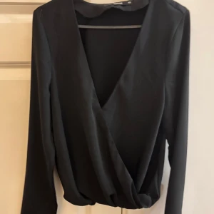Svart omlottopp från BikBok XS - Snygg svart omlottopp från BikBok i storlek XS. Toppen har djup v-ringning och långa ärmar. Perfekt att styla med jeans eller kjol.😍Funkar även bra som S. Använt en gång 