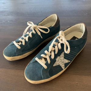 Golden Goose blå mocka sneakers - Snygga sneakers från Golden Goose i blå mocka med vit snörning och glittrig silverstjärna på sidan. Modellen är superstar teal & silver glitter star. Skorna är nästan helt oanvända då jag har ett par likande. Skosnöret är bytt till ett helt nytt. 