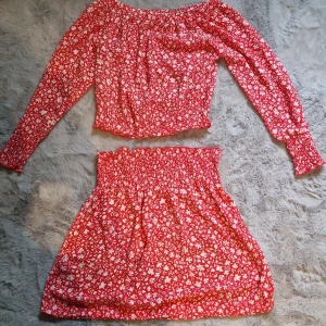 Röd blommig kortkjol med resår - Supersöt röd kortkjol med vitt blommönster och smock i midjan. Kjolen har en luftig och flowy passform, perfekt för varma dagar. Matcha med en enkel topp eller kör hela setet för en extra söt look.