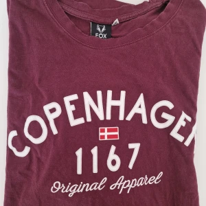 Vinröd t-shirt FOX Copenhagen - Vinröd t-shirt från FOX med tryck 'Copenhagen 1167 Original Apparel' och dansk flagga på bröstet. Skön bomullskänsla och loose fit för en chill vibe.