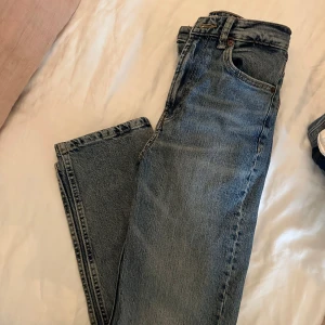 Blå raka jeans från Zara, strl 34 ankellängd - Säljer ett par klassiska blå jeans från Zara i storlek 34. Jeansen har rak passform, hög midja och är tillverkade i bomull. Perfekta till en avslappnad stil och funkar året runt.
