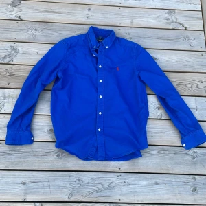 Blå skjorta från Polo Ralph Lauren - Snygg blå skjorta från Polo Ralph Lauren. Storlek är 14-16 år/passar en grabb som är ungefär 160-177 bra, den är nästan som ny,org pris ligger på ungefär 1100kr skriv vid minsta fundering pris är inte hugget i sten
