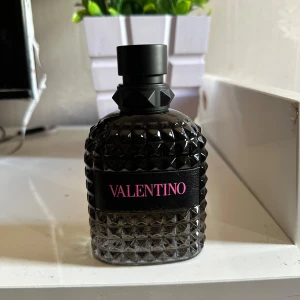 Valentino Uomo Born In Roma EdT 100ml - Exklusiv herrparfym från Valentino, Born In Roma Uomo. Flaskan är mörk och har ett coolt nitat mönster med svart och rosa detaljer. Kommer i en elegant svart kartong med rosa text. Volym: 100 ml. Perfekt för dig som gillar lyxiga och moderna dofter. Kvitto kommer med också 
