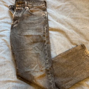 Levis 501 svarta jeans straight fit - Säljer ett par klassiska Levis 501 jeans i svart tvättad denim. Modellen har rak passform, fem fickor och silverfärgade nitar. Ikonisk Levis-lapp bak i midjan och röd etikett på bakfickan. Perfekta för en avslappnad och tidlös look.