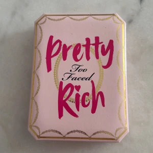 Too Faced Pretty Rich ögonskuggspalett - Säljer en Too Faced Pretty Rich ögonskuggspalett med 16 nyanser i olika finishes, från skimrande guld och silver till matta bruna och rosa toner. Paletten har en lyxig rosa förpackning med spegel och guldiga detaljer. Perfekt för kreativa och glamorösa looks.