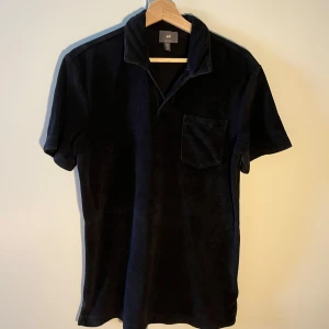 Svart Frottépiké från H&M - Säljer en svart frottépiké från H&M. Pikén har en klassisk passform och är tillverkad i mjukt frotté material. Passar till både linnebyxor och shorts. 