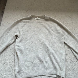 Ljusbeige stickad tröja - En enkel och stilren ljusbeige stickad tröja med rund halsringning och långa ärmar. Perfekt för lager-på-lager och passar till det mesta i garderoben. Ribbstickade muddar vid ärmslut och nederkant.