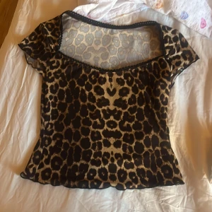 Leopardmönstrad mesh topp - Säljer en leopardmönstrad mesh topp med korta ärmar och rundad halsringning. Toppens material är tunn och genomskinlig mesh i beige och svart, vilket ger en cool och trendig look.