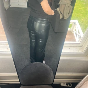 Svarta skinnbyxor med raka ben - Säljer ett par svarta skinnbyxor med raka ben och normal passform. Byxorna har fickor bak och bälteshällor i midjan. Snygg glansig finish som ger en cool look. Perfekta att styla med en enkel topp eller hoodie.