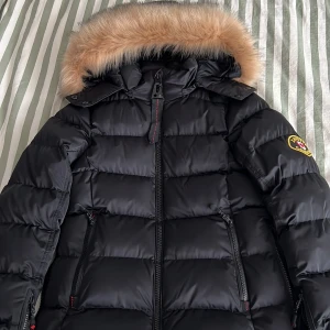 Svart jacka från Zavetti Canada - Säljer en jacka  från Zavetti Canada med avtagbar huva och pälskant. Perfekt för kalla dagar och riktigt snygg stil.