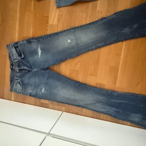 Blå jeans med slitningar från LTB - Säljer ett par blå jeans från LTB med snygga slitningar och tvättade detaljer. Modellen har midwaist och bootcut/flare passform. Perfekta för dig som gillar en klassisk jeanslook med lite extra edge. För mått se bild 4