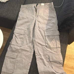 Grå cargobyxor med fickor - Säljer ett par grå cargobyxor med flera stora fickor på sidorna. Byxorna har en rak passform. Perfekta för en avslappnad och trendig stil.
