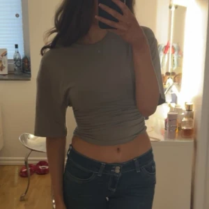 Beige croppad topp med rynkade detaljer - Trendig beige croppad topp med korta ärmar och snygga rynkade detaljer i midjan. Perfekt för en avslappnad och stilren look. Passar bra till jeans eller kjol.