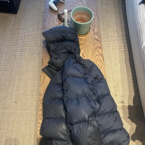 Svart pufferjacka med blått foder från j.lindberg - Säljer en svart pufferjacka med blått foder från J.lindberg . Jackan har huva och dragkedja framtill, samt en quiltad design som håller värmen bra. Perfekt för kyliga dagar och riktigt snygg färgkombination. Köpt för 3900 för 1 år sedan . 