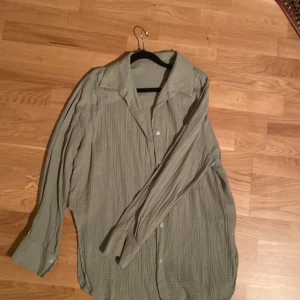 Grå skjorta med knappar - Säljer en grå skjorta med klassisk krage och knäppning framtill. Skjortan har lång ärm och är tillverkad i ett lätt, strukturerat material som ger en avslappnad känsla. Perfekt att styla lager på lager eller bära som den är.