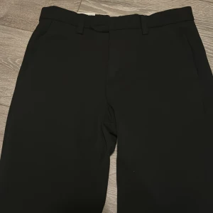 Svarta kostymbyxor från Jack & Jones - Snygga svarta kostymbyxor från Jack & Jones med klassisk passform och raka ben. Byxorna har hällor för bälte, diskreta sidofickor och bakfickor med knappar. Perfekta för en stilren look. 