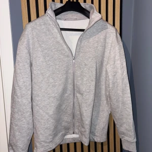 Ljusgrå ziptröja från Lager157 - Säljer en ljusgrå tröja med dragkedja och hög krage. Tröjan har långa ärmar och är i mjukt material, perfekt för lager-på-lager. Enkel och stilren design som passar till mycket.