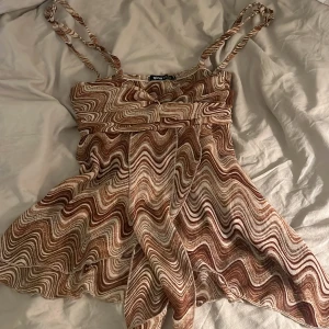 Mönstrad topp från Gina Tricot - Snygg toppen från Gina Tricot med ett vågigt mönster i bruna och beige toner. Klänningen har smala axelband och en fladdrig kjol som ger en härlig rörelse. Perfekt för en somrig look!