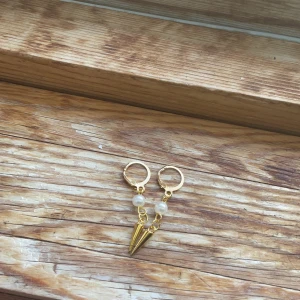 Pearly spike  - Säljer ett par trendiga örhängen i guld med vita pärlor och en konformad hängande detalj. Perfekta för att ge din look en cool och unik touch.