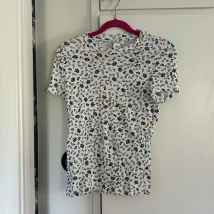 Blommig ribbad t-shirt - Säljer en söt vit ribbad t-shirt från Monki med små blommor i grönt, blått och gult. T-shirten har korta ärmar och rund halsringning. Perfekt för en vårig eller somrig look!🥰bomullsmix.