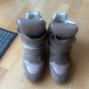  Isabel Marant sneakers - Säljer ett par beige sneakers med kilklack från Isabel Marant. Supersnygga men säljer då de inte riktigt passar. De är i storlek 39 men passar någon mellan 38-39. Super bra skick men säljer billigare då jag ej har äkthetsbevis eftersom jag köpt de second hand!! Skriv för fler bilder, pris går att diskuteras!❣️❣️❣️