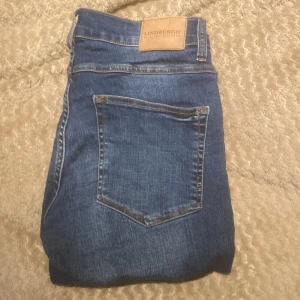 Blå jeans från Lindbergh - Säljer ett par klassiska blå jeans från Lindbergh med normal passform. Jeansen har fem fickor, dragkedja och knapp framtill samt snygga kontrastsömmar. Perfekta till vardags och enkla att matcha med olika outfits.