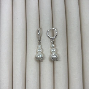 Silverfärgade örhängen med pärlor - Säljer ett par eleganta örhängen i silverfärg med tre vita pärlor i olika storlekar på varje örhänge. Nedre pärlan har en dekorativ detalj i metall. Perfekta för att lyfta din look!