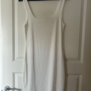 Vit ärmlös klänning - Säljer en enkel och stilren vit klänning med ärmlös design och rundad halsringning. Klänningen har en tight passform och är perfekt för sommardagar eller som basplagg att styla upp eller ner.