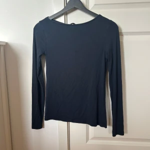 Svart långärmad topp från 157 - En enkel och stilren svart långärmad topp från 157. Modellen har rund halsringning och är tillverkad i ett mjukt material som sitter skönt mot kroppen. Perfekt att matcha med jeans eller kjol.