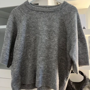Grå stickad tröja från 157 - Mysig grå stickad tröja från 157 med rund halsringning och trekvartsärm. Perfekt för lager-på-lager och enkel att matcha med olika outfits. Klassisk och stilren design.