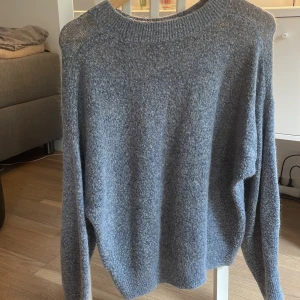 Grå stickad tröja - Mysig grå stickad tröja med rund halsringning och långa ärmar. Perfekt för kyliga dagar och enkel att matcha med olika outfits. Tröjan har en klassisk passform och är tillverkad i ett mjukt material som känns skönt mot huden.