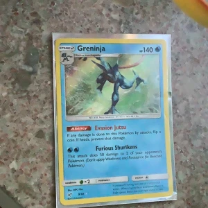 Pokémonkort Greninja - Säljer ett Pokémonkort med Greninja, en vatten-typ Pokémon med 140 HP. Kortet har attacker som Evasion Jutsu och Furious Shurikens. Framsidan har en bild på Greninja i action och baksidan har klassisk Pokémon-design.