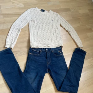 Vit kabelstickad tröja från Ralph Lauren - Säljer en klassisk vit kabelstickad tröja från Ralph Lauren i 100% bomull. Tröjan har rund halsringning, lång ärm och den ikoniska broderade loggan på bröstet. Perfekt för en stilren och tidlös look.