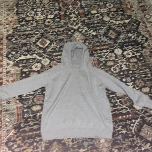 Ljusgrå Kashmir hoodie - En enkel och stilren ljusgrå kasmir hoodie med huva. Tröjan har långa ärmar och ribbade muddar vid ärmslut och nederkant. Perfekt för en avslappnad look.