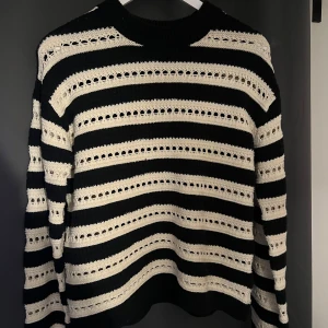 Svart och vit randig stickad tröja från H&M - Säljer en svart och vit stickad tröja från H&M i storlek XS. Tröjan har ett randigt mönster med hålstickade detaljer och långa ärmar. Perfekt för lager-på-lager och ger en cool, avslappnad look.
