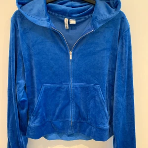 Blå velour hoodie med dragkedja från UNIQLO - Mysig blå hoodie i velour från UNIQLO med dragkedja framtill och huva. Jackan har långa ärmar och en stor ficka på magen. Perfekt för en avslappnad och trendig look.