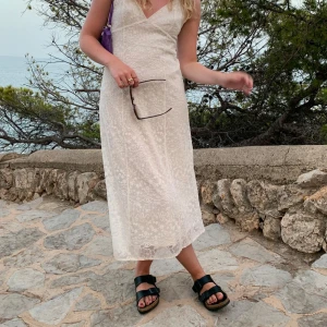 Vit spetsklänning med smala axelband - Säljer en romantisk vit långklänning med smala axelband och v-ringning. Klänningen har ett fint spetsmönster över hela och är fodrad upptill. Perfekt för sommarens alla tillfällen.