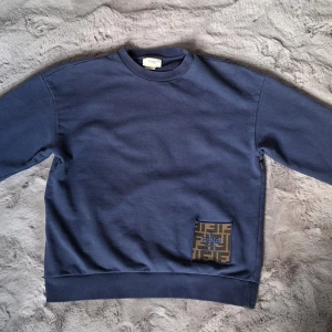 Fendi sweatshirt stl 12 år - Säljer en blå sweatshirt från Fendi med en stor broderad logotyppatch framtill. Tröjan har rund halsringning och är tillverkad i mjuk bomull. Perfekt för dig som gillar exklusiva märken och stilren design. Inköpt sommaren 2024 på NK i Göteborg. Nypris 4200 kr.
