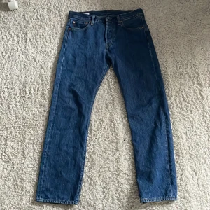 Levi's 501 blå jeans - Hej! Säljer ett par klassiska blå Levi's 501 jeans med rak passform och fem fickor. Byxorna har knappgylf och är tillverkade i slitstarkt denim. Perfekta för en tidlös och avslappnad stil.